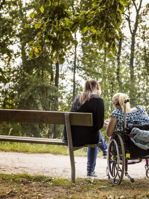 Disabled woman in wheelchair with assistant in park